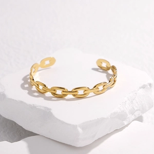 Dettaglio del bracciale rigido aperto a catena dorata su una pietra decorativa bianca