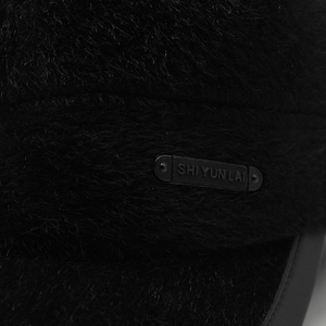 Macro shot of faux mink fur texture and a metallic logo plaque on the black winter hat