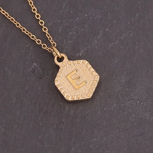 Macro shot of gold hexagonal pendant featuring an embossed letter E with sunburst texture