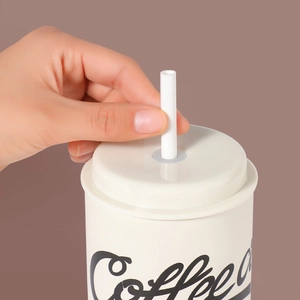 Primo piano di una mano che inserisce una cannuccia bianca in una tazza da caffè con coperchio
