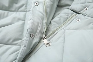 Detail of light mint green quilted jacket featuring silver zipper and metal snap closure