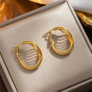 Twisted gold titanium steel C-shaped hoop earrings on gray velvet jewelry display
