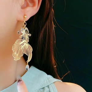 Detailed close-up of golden hollow koi fish earrings with crystal beads on a model