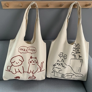 Cute canvas tote bag with hand-drawn cat illustration hanging on a wooden wall hook