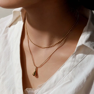 Close-up of double-layer gold necklace with snake chain and teardrop pendant on model