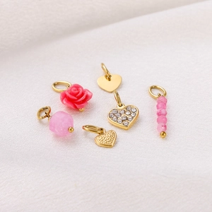 Detail view of heart-shaped gold pendants and pink rose charms on textured fabric