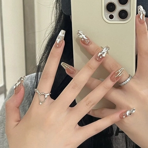 Detail of nude press-on nails with silver 3D accents and rhinestones in long coffin shape
