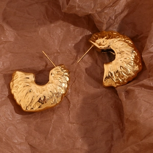 Macro shot of 18K gold plated fan-shaped earrings with hammered texture on paper