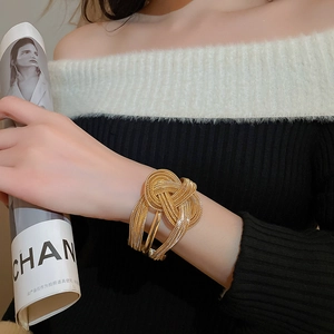 Detail of a gold braided chain open cuff bracelet worn by a model in a fashion setting