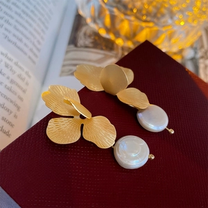 Detailed close-up of golden matte flower petal earrings featuring a white pearl drop