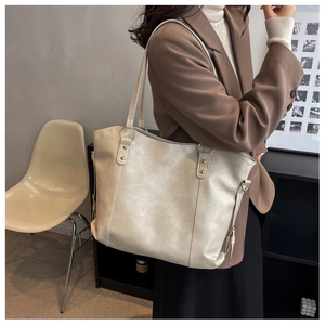 Detail of a large cream tote bag featuring soft leather texture and golden metal hardware