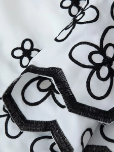 Close-up of black floral embroidery and scalloped edge on white cotton resort shirt