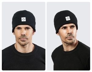 Close-up of black ribbed knit beanie featuring a minimalist white smiley face patch