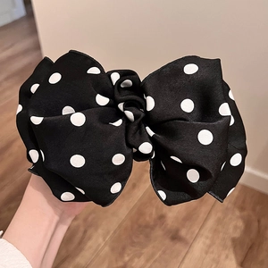 Close-up of a large black bow hair clip with white polka dots made of thick matte fabric