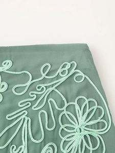 Gros plan détaillé d'une broderie florale vert clair sur le tissu texturé d'une jupe de vacances