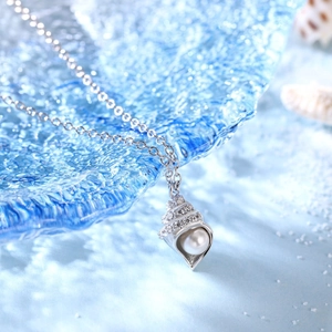 Detail showing a conch shell pendant with white pearl and sparkling crystals on a silver chain