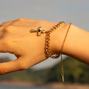 Close-up of gold Cuban chain bracelet with black stone cross pendant worn in sunset light
