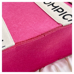 Close-up of pink felt tote bag material with high-density stitching and lettered straps