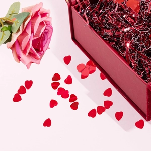 Macro view of red heart glitter and sequins inside a gift box with a pink rose