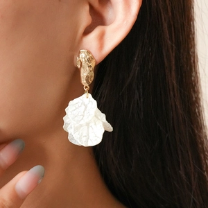 Close-up of bohemian acrylic petal earrings with gold textured metal and white tassels