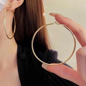 Close-up of stylish large gold hoop earrings worn and held to show scale and texture
