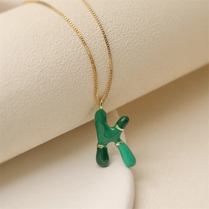 Collana a catena dorata con ciondolo lettera K in smalto verde su sfondo beige