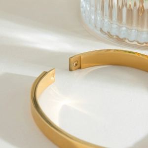 Dettaglio macro del bracciale rigido dorato con chiusura a scatto e finitura lucida