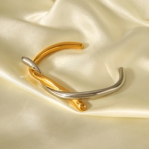 Detail of gold and silver mixed color knotted stainless steel open cuff on silk background