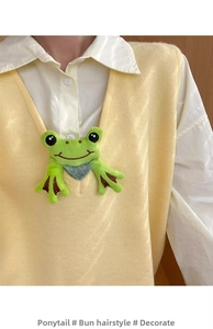 Detail of cute green plush frog hair tie accessory pinned to a yellow knit vest