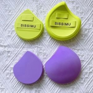 Detail view of yellow and purple makeup sponges with ribbon strap on woven fabric background