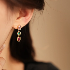 Detail von Vintage-Goldohrringen mit lila, grünen und roten Edelsteinen am Model