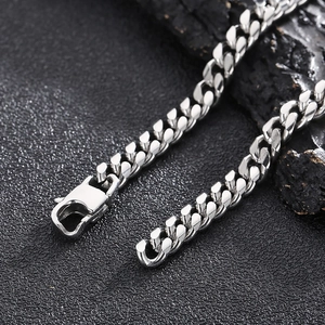 Macro shot of silver Cuban chain necklace with lobster clasp on dark textured rock surface