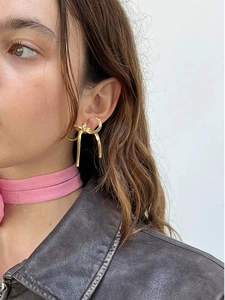 Minimalist 18K gold bow tassel earring worn by a model against a white wall background