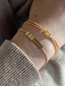 Detail of gold Mobius knot bracelet and engraved 'always on my mind' bar bracelet on wrist