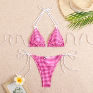 Detail of pink gingham bikini with white side ties and bow accents on sandy beach background