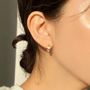 Close-up of a minimalist gold hoop earring with a white pearl on a model's ear