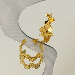 Detailed view of gold geometric earrings with textured surface on a reflective surface