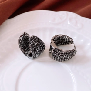 Detailed view of asymmetric hoop earrings with black zircon stones on a white ceramic tray