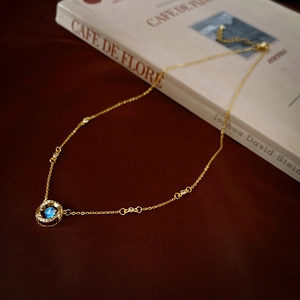 Élégant collier doré avec pendentif en zircon bleu et détails scintillants sur livre rétro