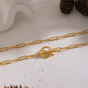 Close-up of golden paperclip chain necklace with toggle clasp on stone background