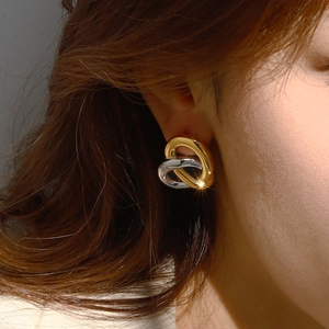 Elegant two-tone intertwined heart stud earrings with a polished mirror finish on model