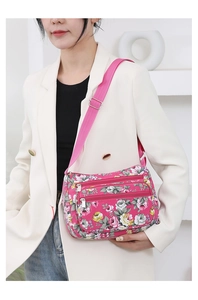 Detail of pink floral nylon crossbody bag featuring multi-zipper compartments and strap