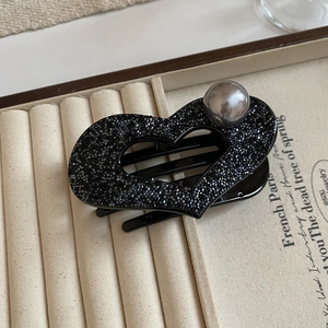 Detail of heart hair claw with black crystals and pearl on a beige velvet jewelry box