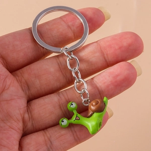 Cute green snail keychain with brown shell on silver ring held against pink background