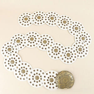 Detailed macro view of retro white leather belt discs with bohemian floral metal carvings
