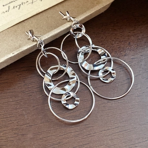 Silver geometric hollow hoop earrings with layered hammered texture on wood surface