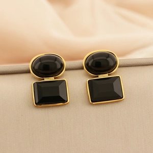 Macro detail of elegant black and gold geometric earrings on smooth beige texture