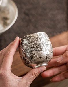 Gros plan d'une tasse à thé dragon en argent 999 montrant des gravures et texture vintage