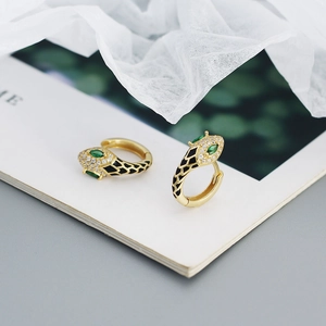 Detailed view of gold snake hoop earrings with black enamel and green zircon eyes