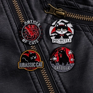 Detailed view of four funny cat enamel pins pinned onto a black leather punk jacket